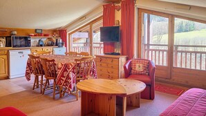 Quarto aconchegante com mesa de jantar, cadeiras, sofá, televisão e área de cozinha equipada.