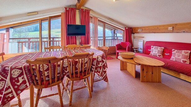 Um quarto acolhedor com uma mesa de jantar, cadeiras, um sofá vermelho e uma televisão.