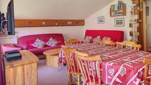 Um quarto aconchegante com um sofá vermelho, cadeiras de madeira, uma mesa pequena e uma cama com colcha estampada.