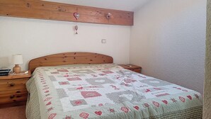 Quarto com cabeceira de madeira, colcha acolchoada, mesa de cabeceira com abajur e criado-mudo pequeno.