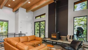 A modern interior with a leather sofa, a black leather chair, a fireplace, and large windows offering views of greenery. - Cliff and Canopy - Lakefront Masterpiece w/Private Dock (Bonner County)