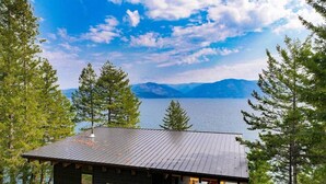 A cabin with a metal roof overlooking a lake and mountains. - Cliff and Canopy - Lakefront Masterpiece w/Private Dock (Bonner County)