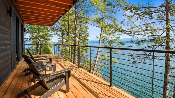 A wooden deck with picnic tables overlooking a lake, surrounded by trees. - Cliff and Canopy - Lakefront Masterpiece w/Private Dock (Bonner County)
