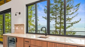 A modern kitchen with a large window offering a scenic view of trees and water. - Cliff and Canopy - Lakefront Masterpiece w/Private Dock (Bonner County)