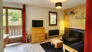 Een gezellige woonkamer met een houten dressoir, een televisie, een open haard en een raam met uitzicht op groen.