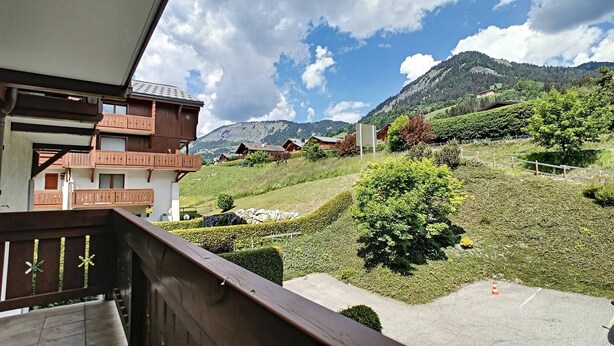 Uitzicht op bergen met een houten balkon dat uitkijkt over een verzorgde tuin en een rij traditionele huizen.