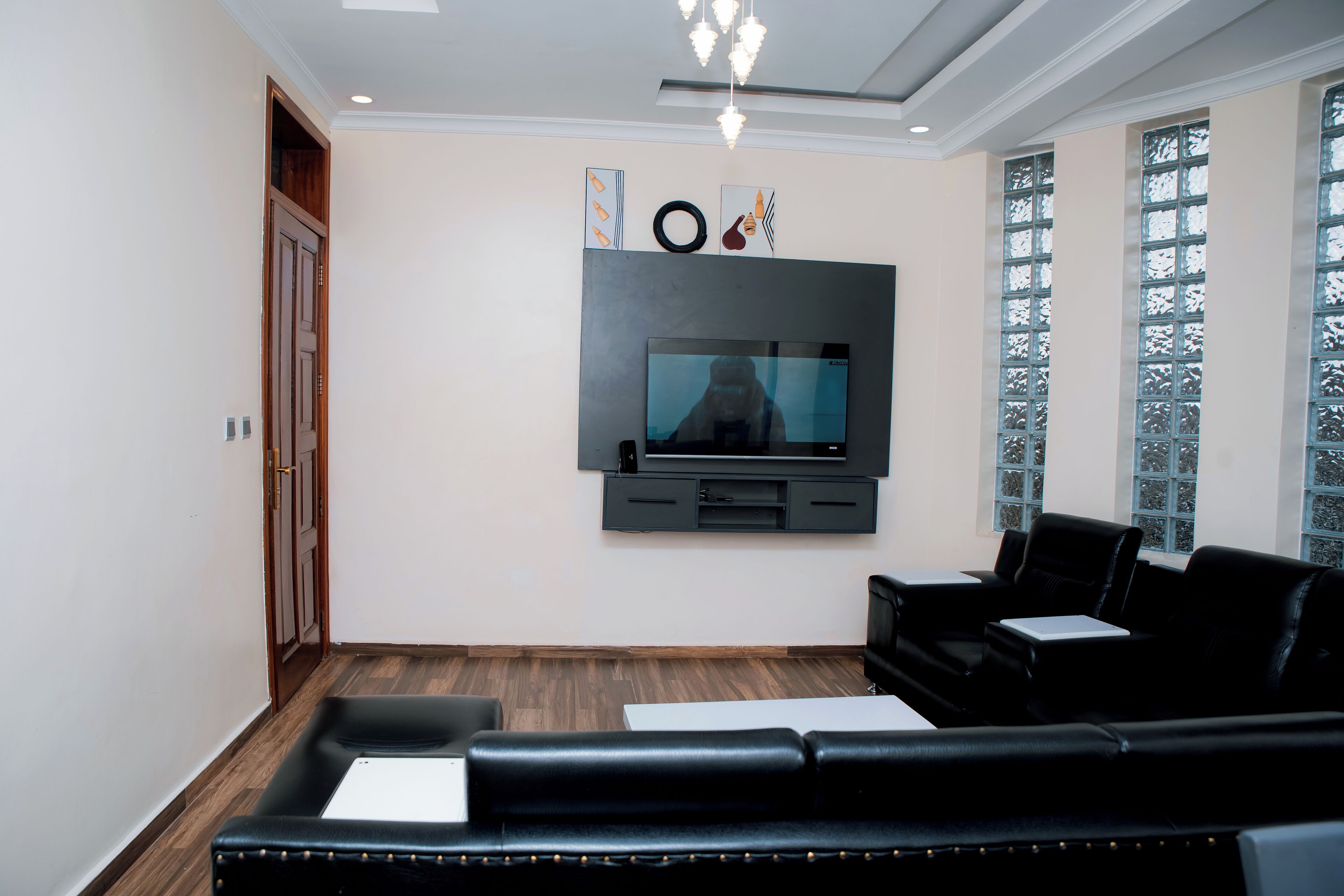Een moderne woonkamer met een flatscreen televisie aan de muur, een zwarte leren bank en een houten vloer.
