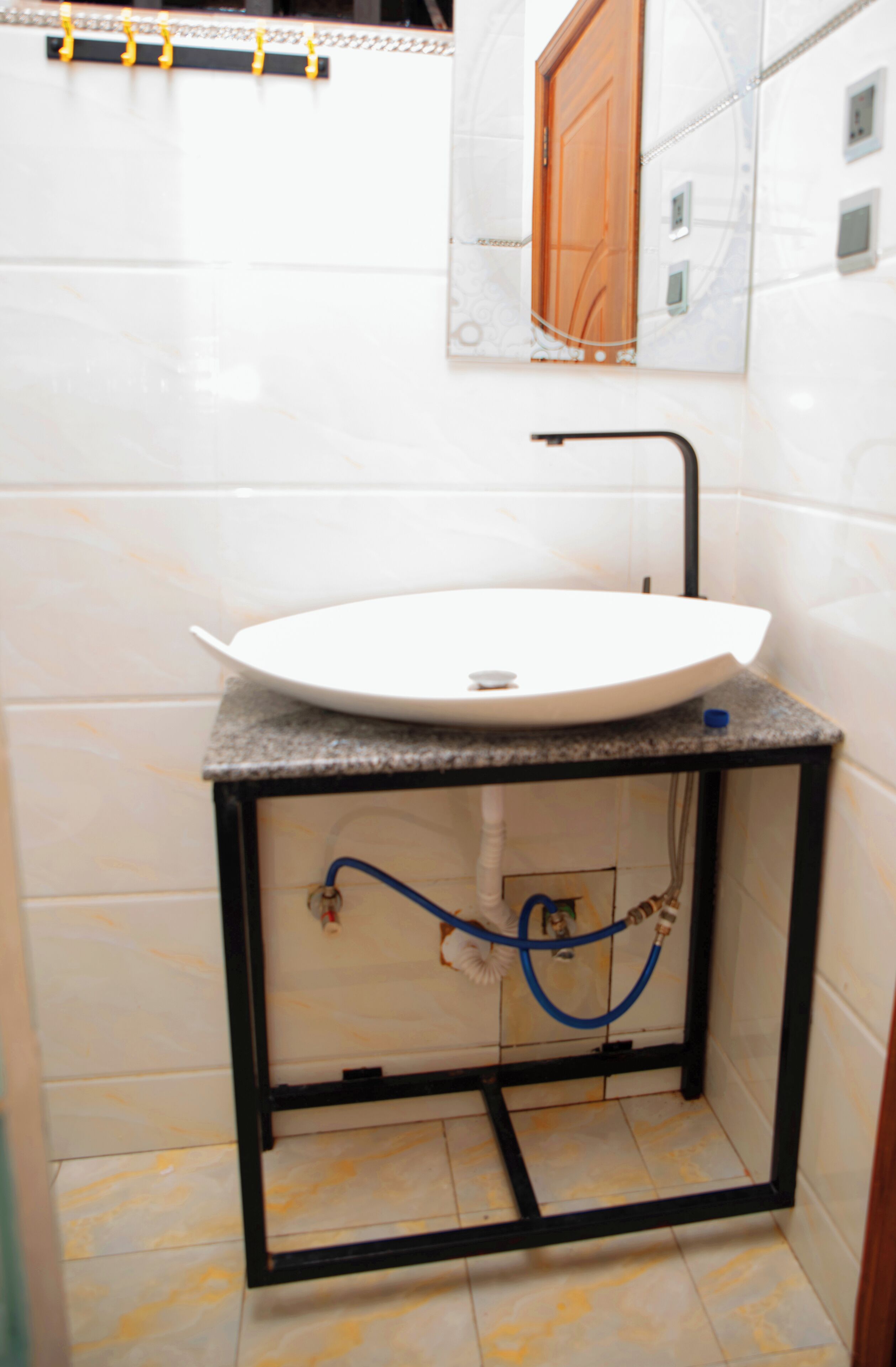 A bathroom with a white sink on a black metal frame, a mirror above it, and a door with a wooden panel.