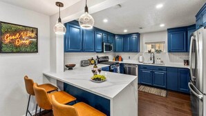A modern kitchen with blue cabinets, a central island with bar stools, stainless steel appliances, and pendant lighting. - The Copper Cottage: An Eclectic Oasis with Hot Tub (Berkley)