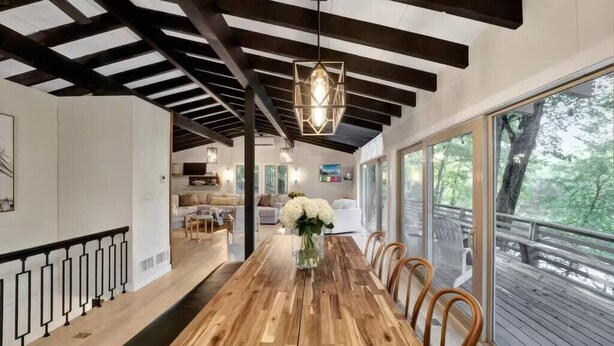 Un comedor amplio con una larga mesa de madera, barandas de metal negro y grandes ventanales con vistas al exterior.