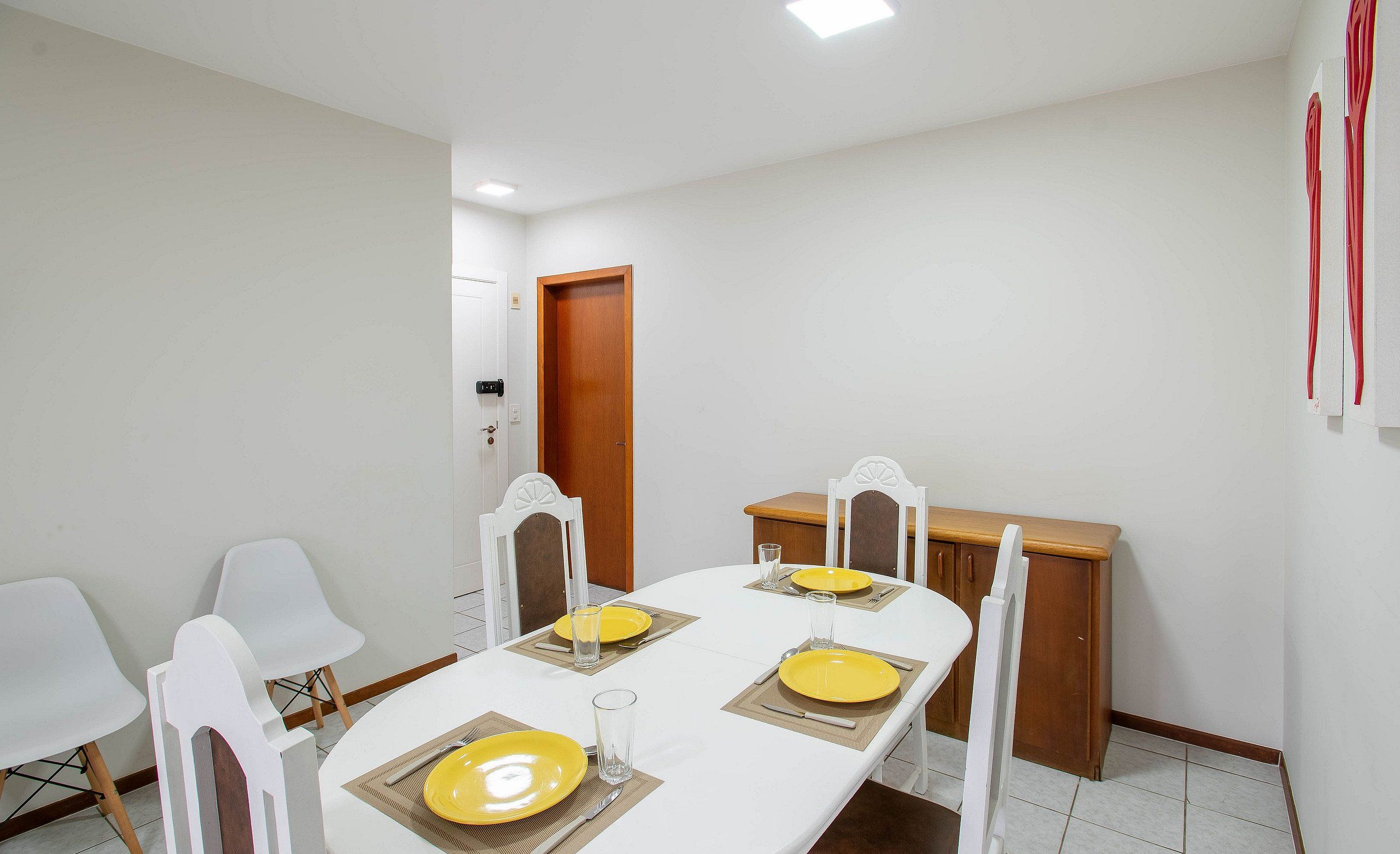 A dining area with a white table set for four, white chairs, and a wooden cabinet.