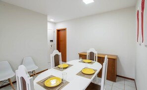 A dining area with a white table set for four, white chairs, and a wooden cabinet. - Apartment w/ Barbecue 350m From the Beach Ilh0503 (Balneário Camboriú)