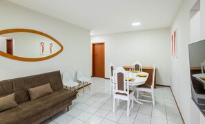 A living room with a brown sofa, white chairs, a dining table, and a TV. - Apartment w/ Barbecue 350m From the Beach Ilh0503 (Balneário Camboriú)