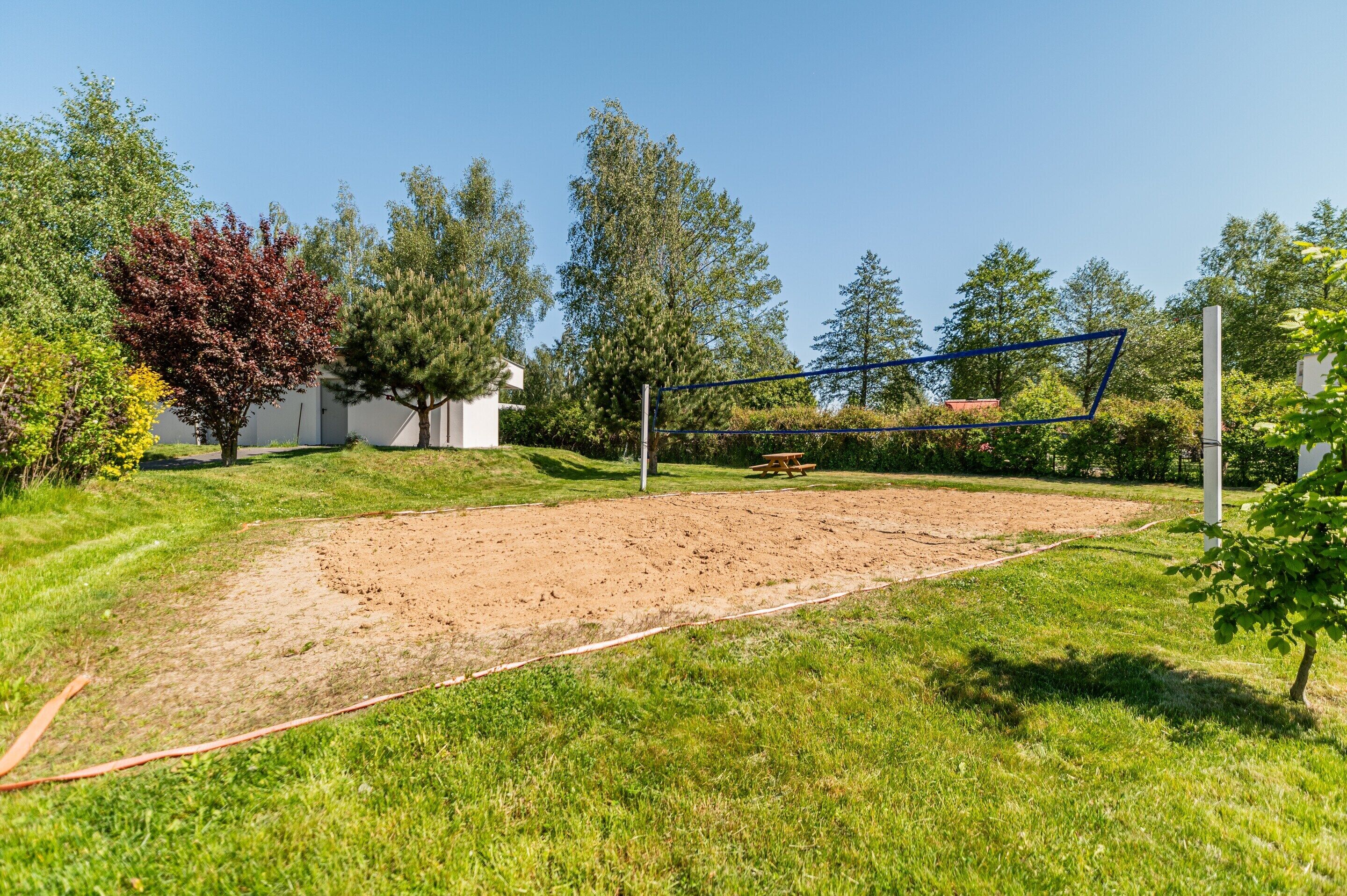 A volleyball court with a net, surrounded by grass and trees.