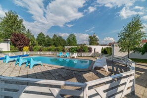 Une piscine entourée de chaises bleues, délimitée par une clôture blanche, avec des arbres en arrière-plan.
