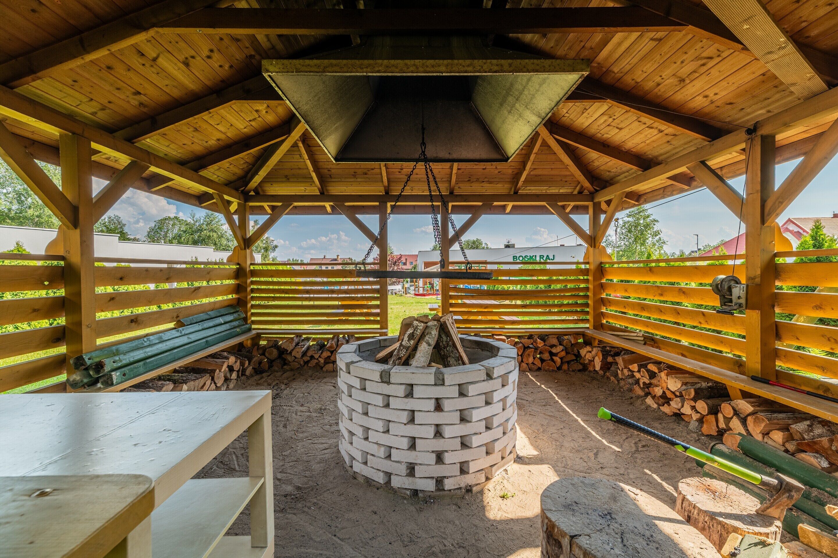 A covered outdoor area with a central fire pit, benches, and stacked firewood.