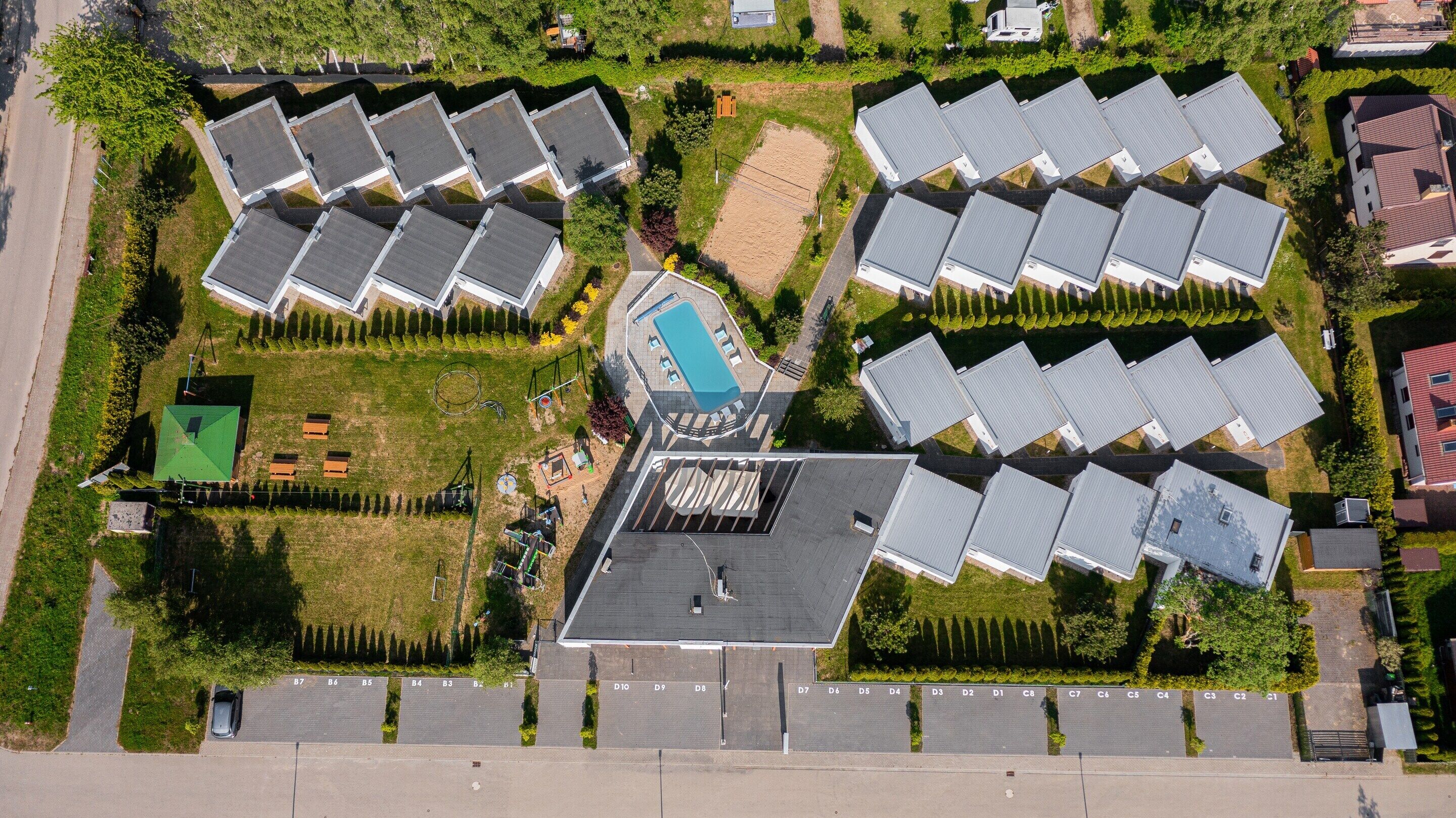 An aerial view of a residential area with multiple detached houses, a central swimming pool, and a well-maintained lawn.