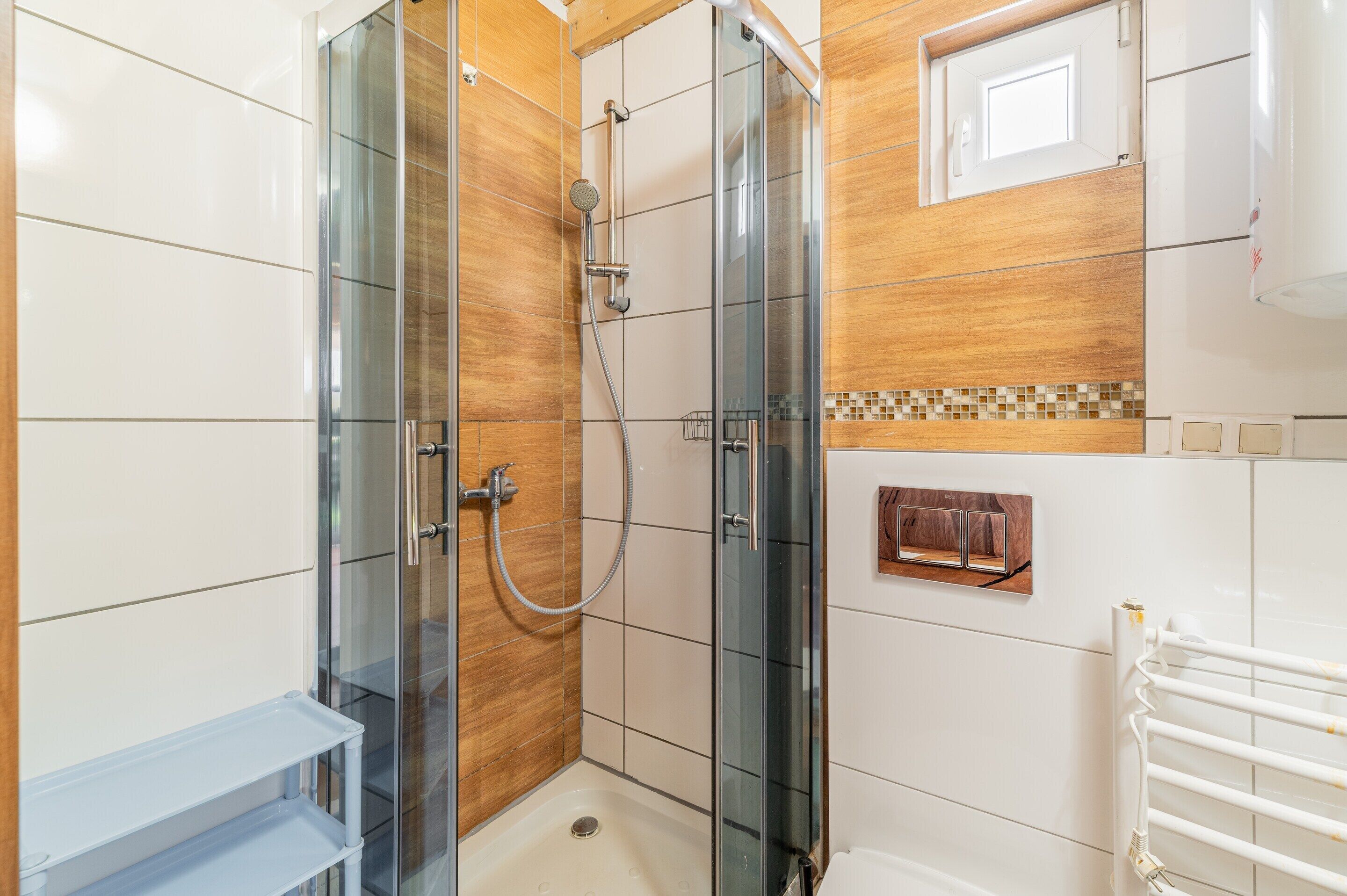 A modern bathroom with a glass-enclosed shower, white tiles, and a wooden accent wall.