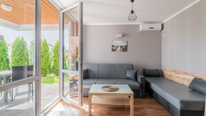 A modern living room with a grey sofa, a wooden coffee table, and a glass door leading to an outdoor area with a patio table and chairs. - Comfortable Holiday Homes Near the Sea, Pool (Ustronie Morskie)