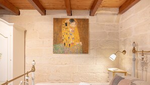 A bedroom with a bed, a nightstand, a lamp, a painting, and a wooden ceiling. - La Dimora di Marco – Exclusive Art Rooms in Salento (Melendugno)