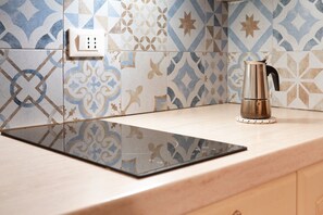A kitchen with patterned tiles, a black induction cooktop, and a stainless steel kettle on a light-colored countertop.