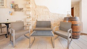 A stone wall, wicker chairs, a table, and a wooden barrel in a room. - La Dimora di Marco – Exclusive Art Rooms in Salento (Melendugno)
