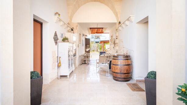 A corridor with a stone archway, a wooden barrel, wicker planters, and a white cabinet with a glass door. - La Dimora di Marco – Exclusive Art Rooms in Salento (Melendugno)
