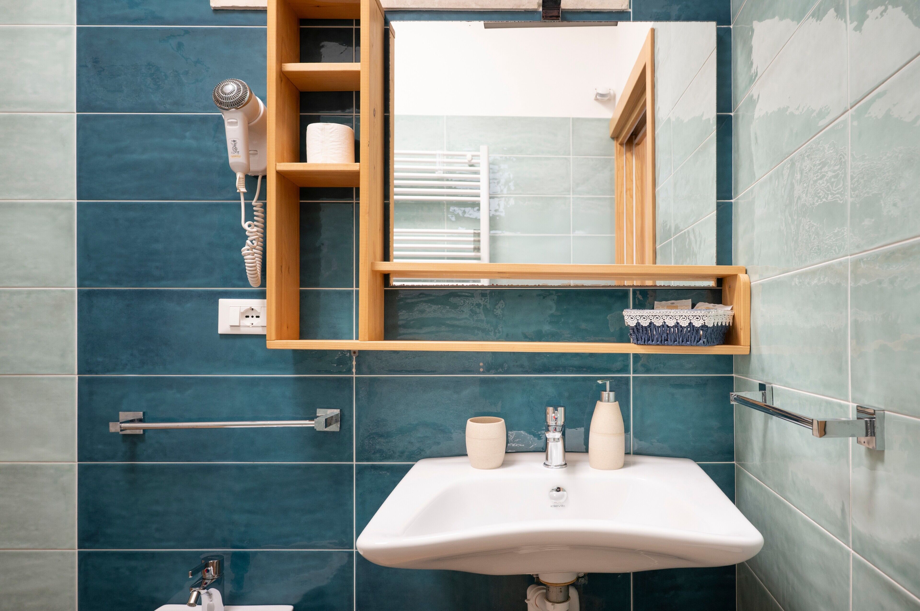 A bathroom with a sink, mirror, towel rack, and a hairdryer mounted on the wall.