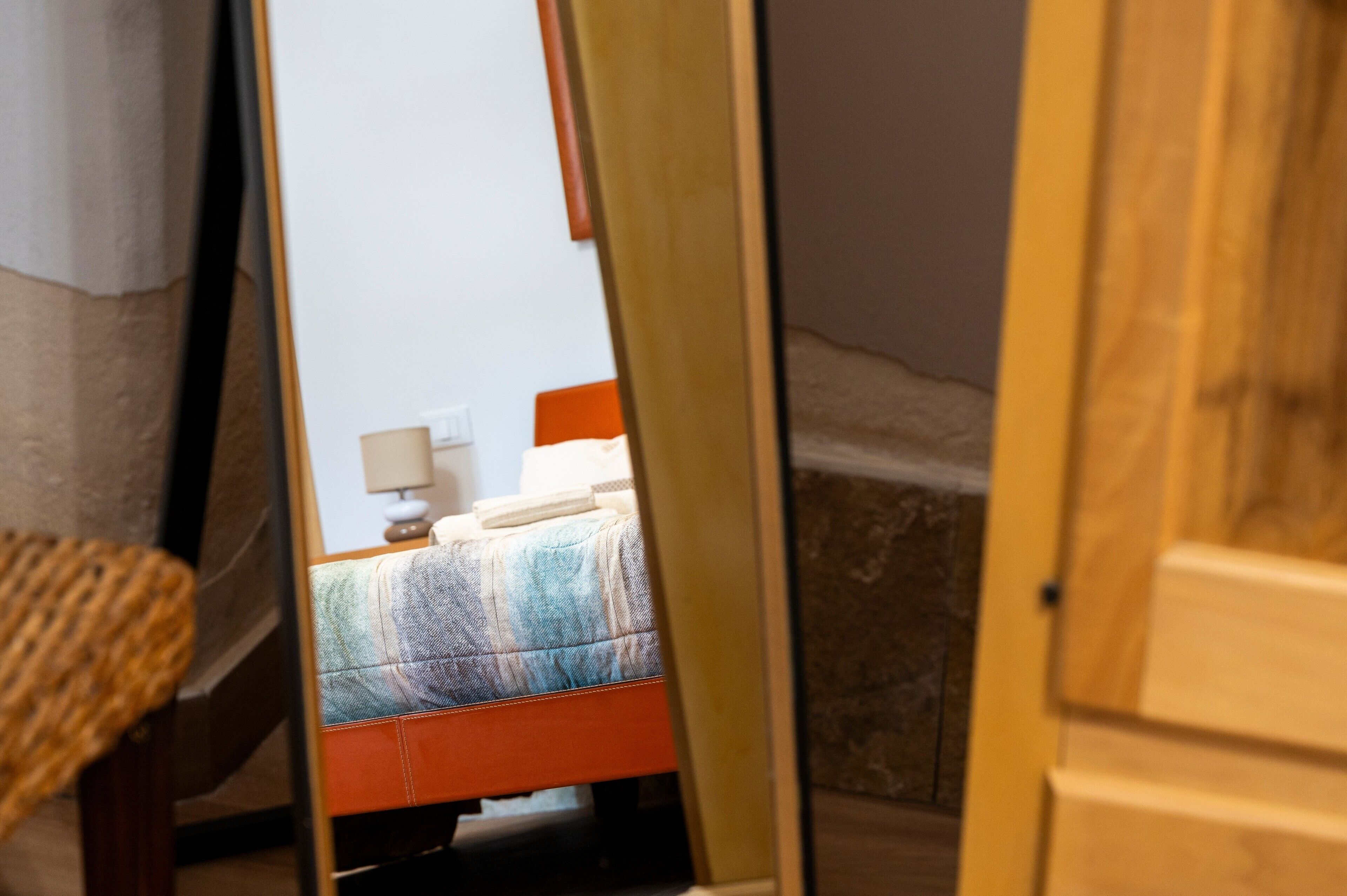 Ein Zimmer mit einem Bett, einem Nachttisch und einem Spiegel, der das Zimmer reflektiert.