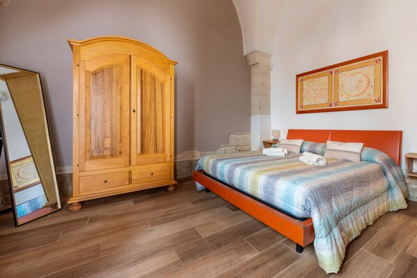 Ein Schlafzimmer mit einem Holzschrank, einem Bett mit gestreifter Bettdecke, einer Steinwand und einem gerahmten Kunstwerk über dem Bett.