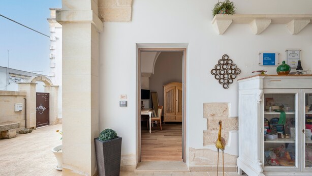 A hallway with a wooden floor, a white cabinet with glass doors, and a door leading to a room with a chair and a table.