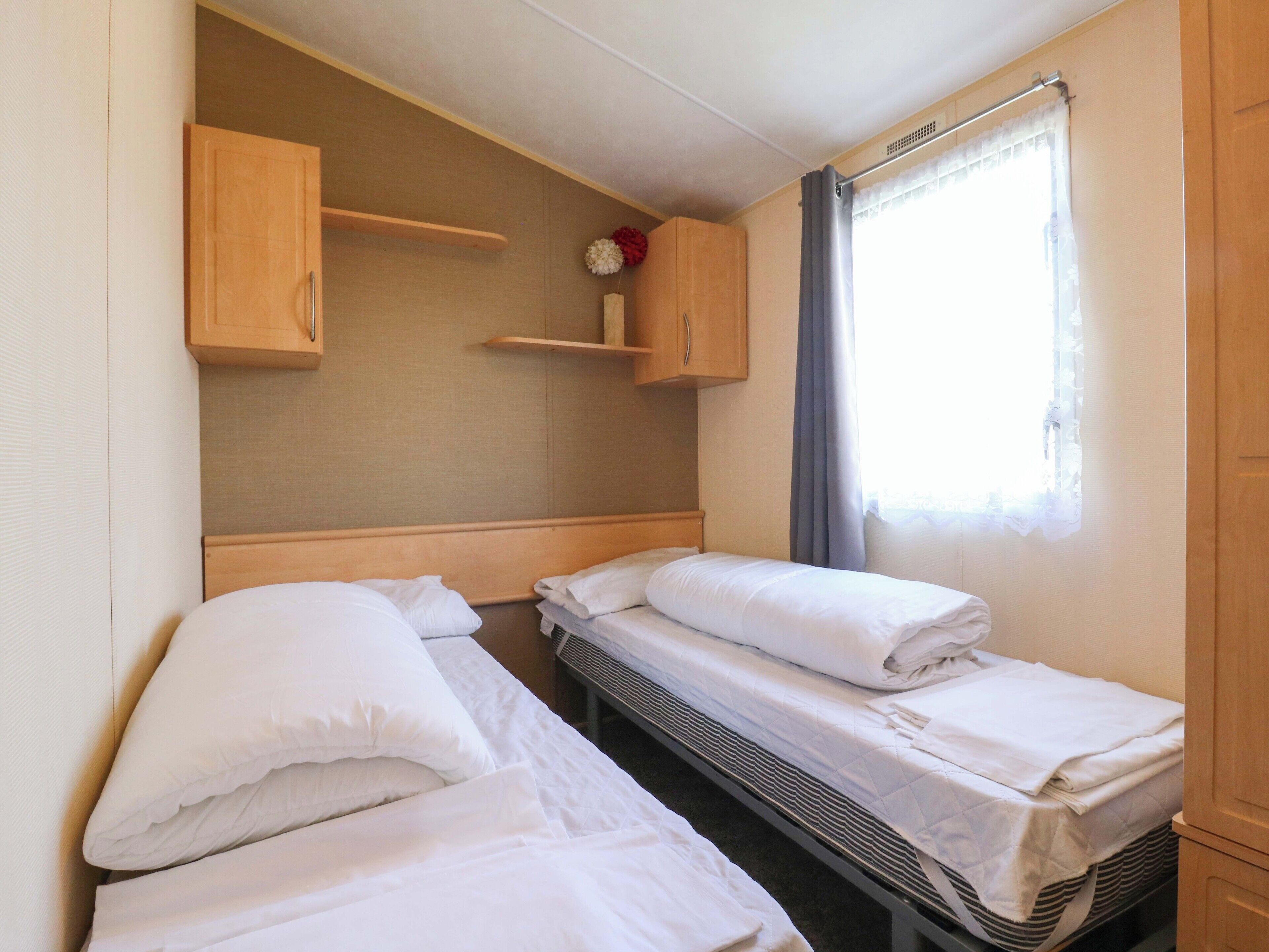 Una habitación pequeña con dos camas individuales, un armario de madera y una ventana con cortinas.