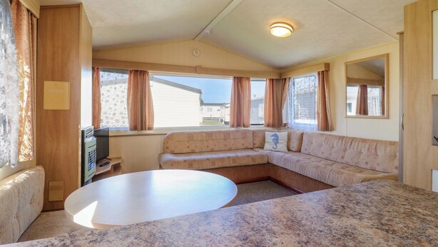 A compact living area with a sectional sofa, a small table, and a television. - Singh Leite &amp; Luisa Family Caravan (Clacton-on-Sea)