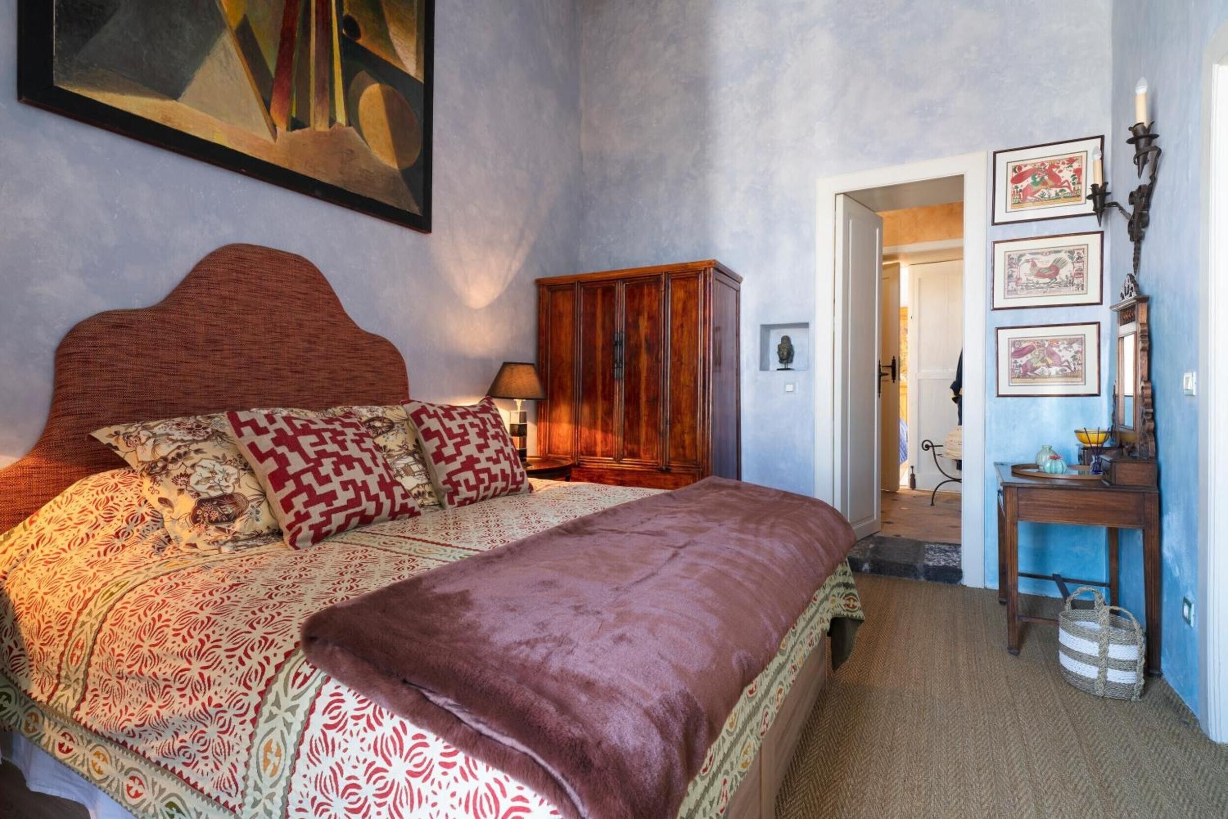 A bedroom with a large bed, a wooden wardrobe, and a painting on the wall.