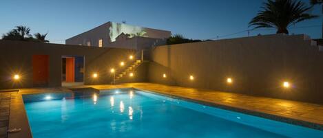 A swimming pool with steps leading to a building, surrounded by walls and a palm tree.