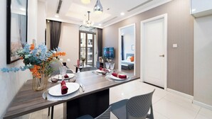 A modern dining area with a wooden table set for four, a vase with flowers, and a television in the background. - The Landmark Residence Of Central City (Ho Chi Minh City)