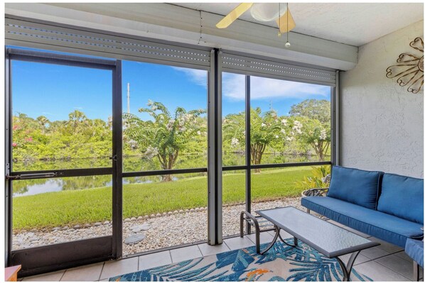 A room with a large sliding glass door leading to a lush garden, a blue sofa, and a small table.