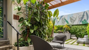 A modern outdoor seating area with a concrete floor, surrounded by lush greenery and a decorative wall.