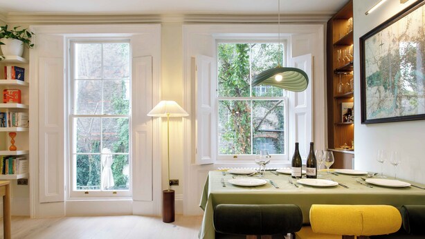 Un coin repas avec une table dressée pour quatre personnes, une lampe et une vue sur la verdure à l’extérieur.