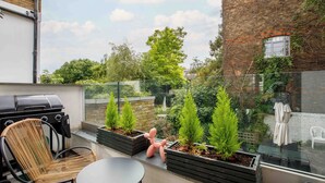 Une terrasse sur le toit équipée d’un barbecue, de sièges et de plantes en pot.