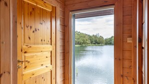 A wooden cabin interior with a large door leading to a lake view.