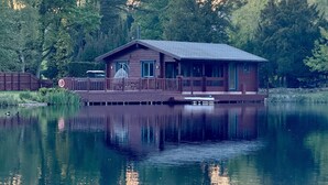 A wooden cabin with a dock, surrounded by a forest and a calm lake.