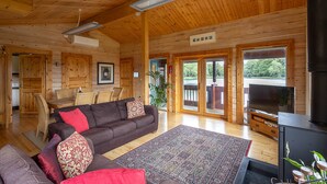 A wooden cabin interior with a sofa, TV, and dining area.