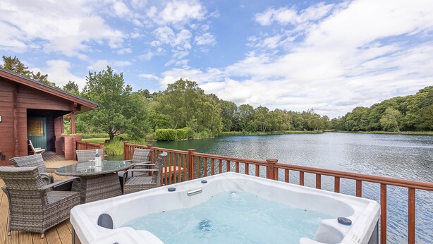 A deck with a hot tub, wicker furniture, and a view of a lake.