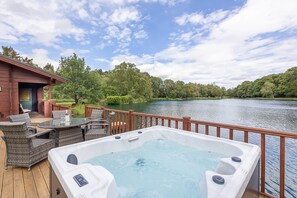 A deck with a hot tub, wicker furniture, and a view of a lake. - JEM Lodge - Lakeside Farm Ltd (Stocksfield)