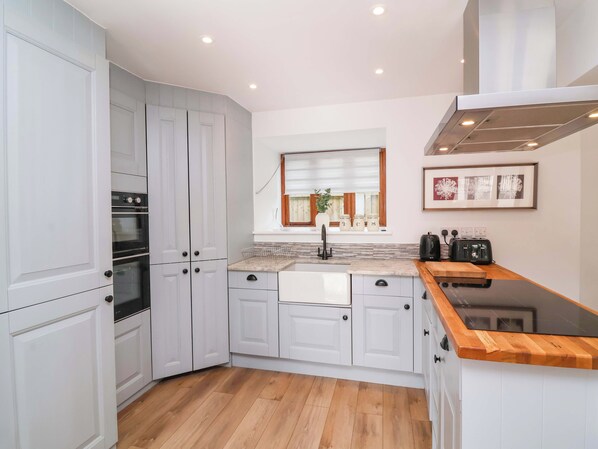 A modern kitchen with white cabinetry, a wooden countertop, and a built-in oven. - Butterfly Days (Bideford)