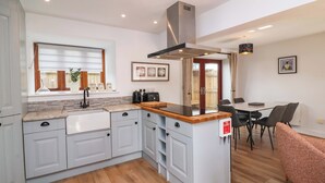 A modern kitchen with grey cabinets, a wooden countertop, and a built-in island. There is a dining area with a table and chairs, and a fire blanket on the island. - Butterfly Days (Bideford)