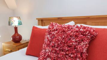 Un lit avec un oreiller rouge et blanc à texture particulière, une table de chevet en bois avec une lampe, et une tête de lit en bois.