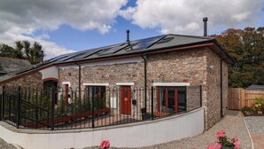 A stone building with a curved balcony, solar panels, and a chimney. - Butterfly Days (Bideford)