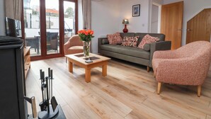 A living room with a sofa, two armchairs, a coffee table with a vase of flowers, a television, and a sliding glass door leading to an outdoor area. - Butterfly Days (Bideford)